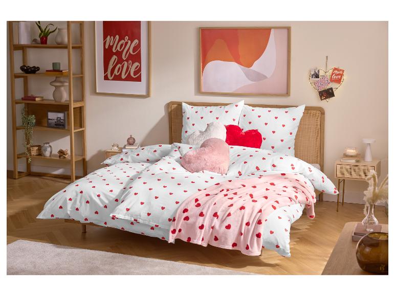 Chambre avec lit double, parure de lit blanche à cœurs rouges et coussins en forme de cœur.