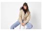 Femme en doudoune beige, jean bleu clair et bonnet vert olive