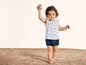 Un bébé fille portant un haut fleuri et un short, tenant un ballon.