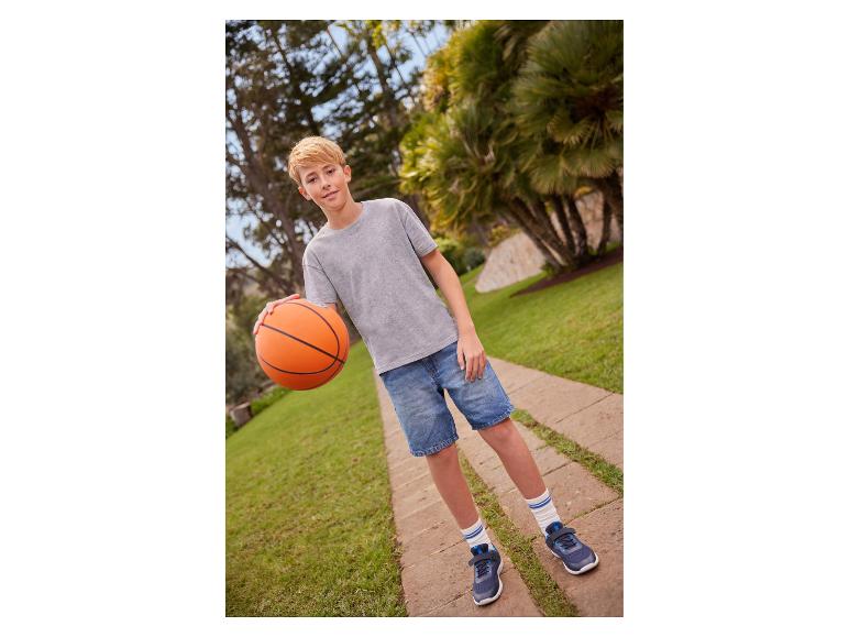Garçon en t-shirt gris et short en jean tenant un ballon de basket sur un chemin.