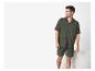 Man in groene mousseline pyjama, overhemd en korte broek, lachend en opzij kijkend.