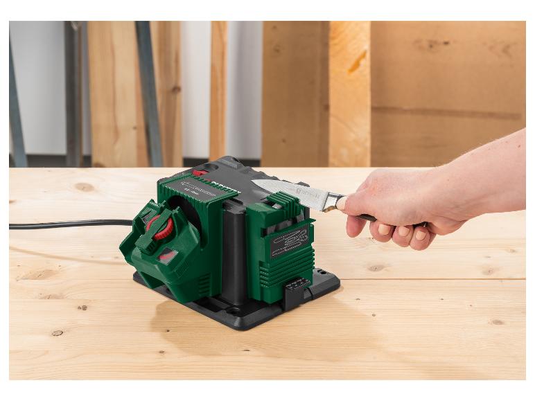 Affûteur électrique vert et noir affûtant un couteau de cuisine sur une table en bois.