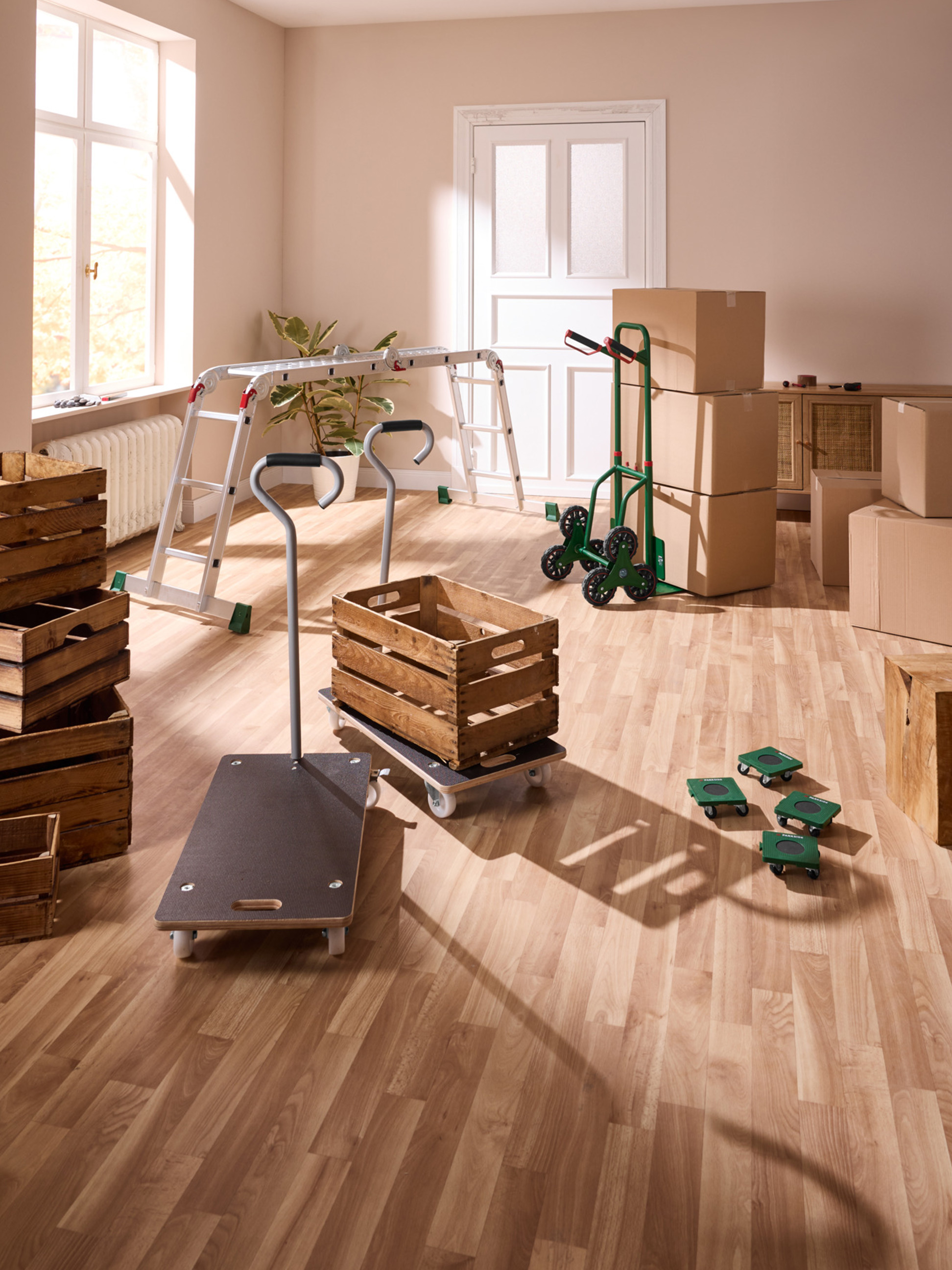 Transportkarren en houten kisten in een kamer met parket, klaar voor een verhuizing.