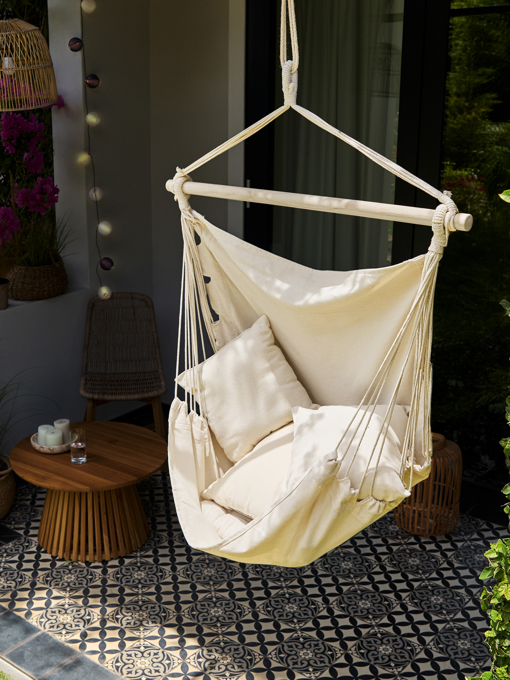 Chaise hamac en tissu crème avec coussins, table en bois et carrelage à motifs sur un balcon.