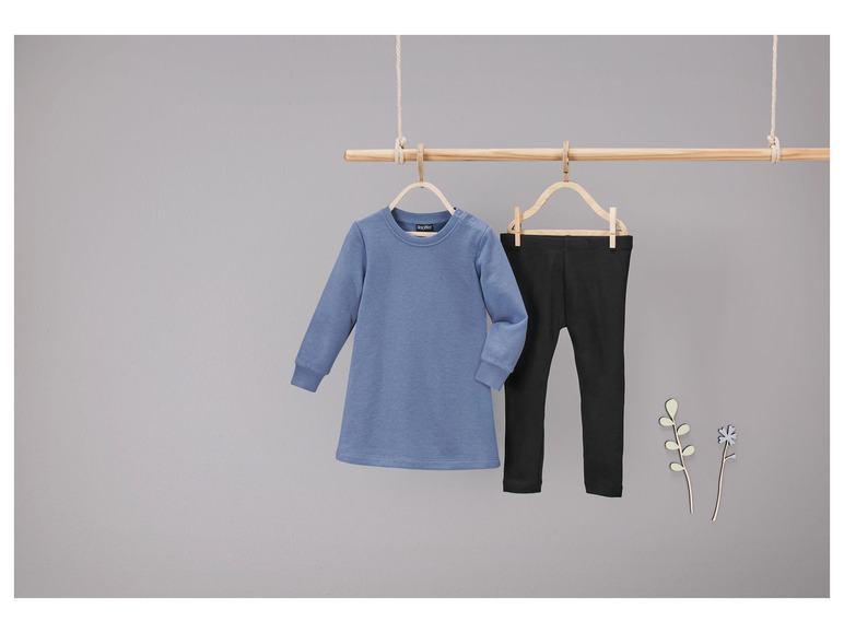 Een blauwe longsleeve en zwarte leggings hangen aan een houten rek.