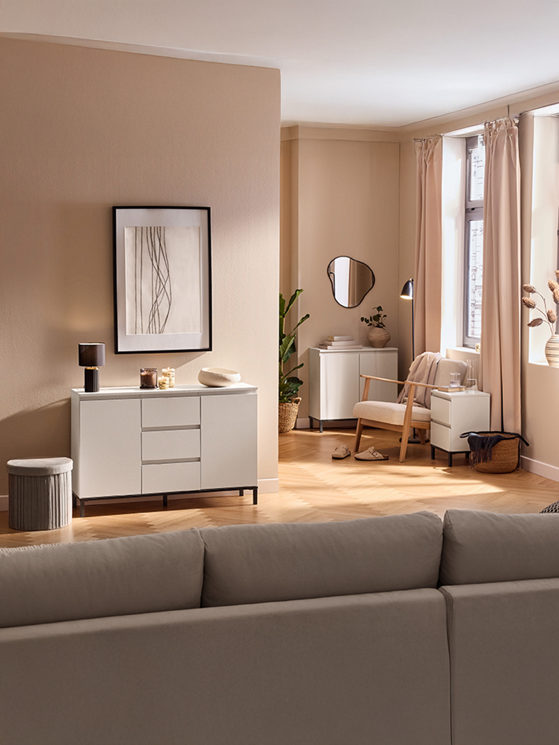 Woonkamer met beige muren, wit dressoir, fauteuil en bank.