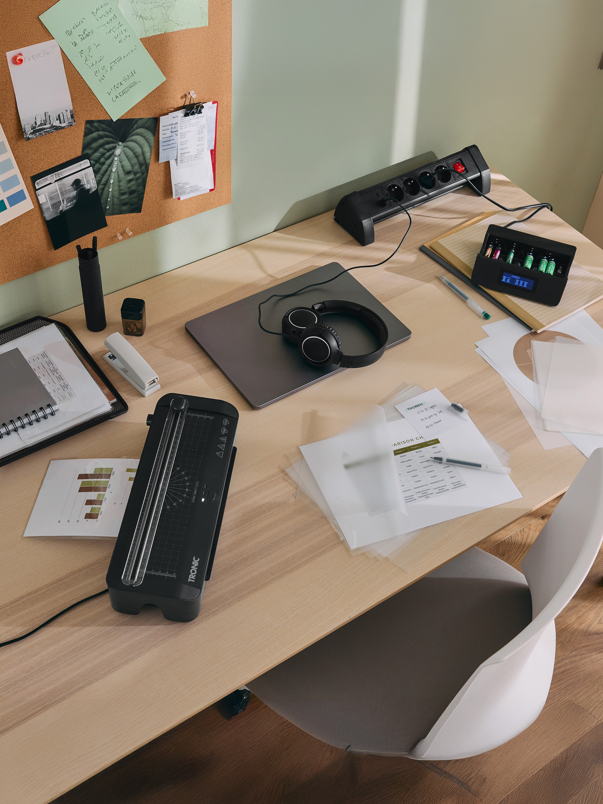 Bureau avec plastifieuse TRONIC, chargeur de piles, ordinateur portable, casque et fournitures de bureau.