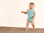 Een baby in een blauwe romper met bloemenprint loopt op een vloerkleed.