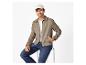 Man in een beige jas, wit t-shirt, jeans en een beige pet, zittend op een kruk.