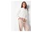 Femme en chemise blanche brodée et pantalon large beige clair.