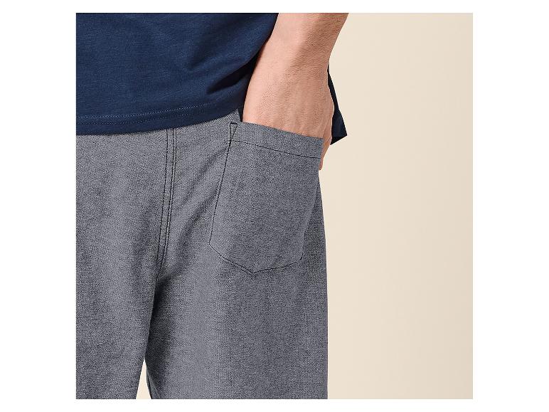 Homme en t-shirt bleu et short gris, main dans la poche.