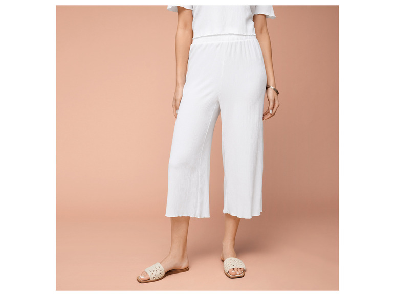 Witte broek met wijde pijpen en sandalen met gevlochten bandjes.