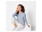 Een vrouw draagt een blauwe trui en witte broek.