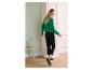 Femme en pull tricoté vert et pantalon noir avec des baskets à l'intérieur.