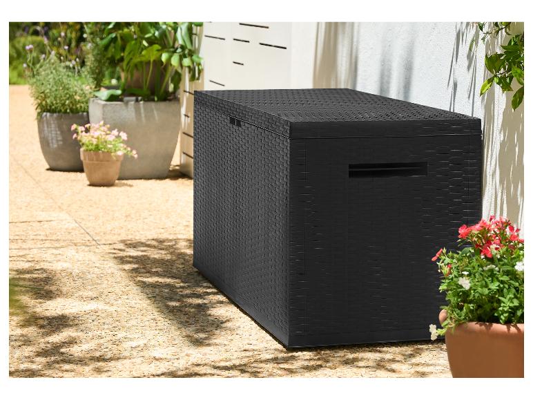 Boîte de rangement noire aspect rotin sur une terrasse avec des plantes en pot.