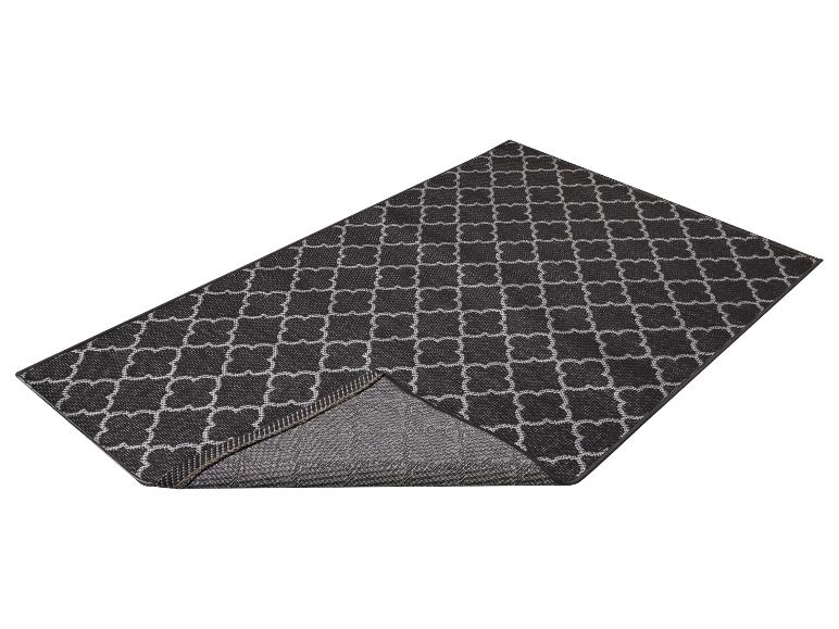 Tapis de sol noir avec motif géométrique blanc, un coin est plié.