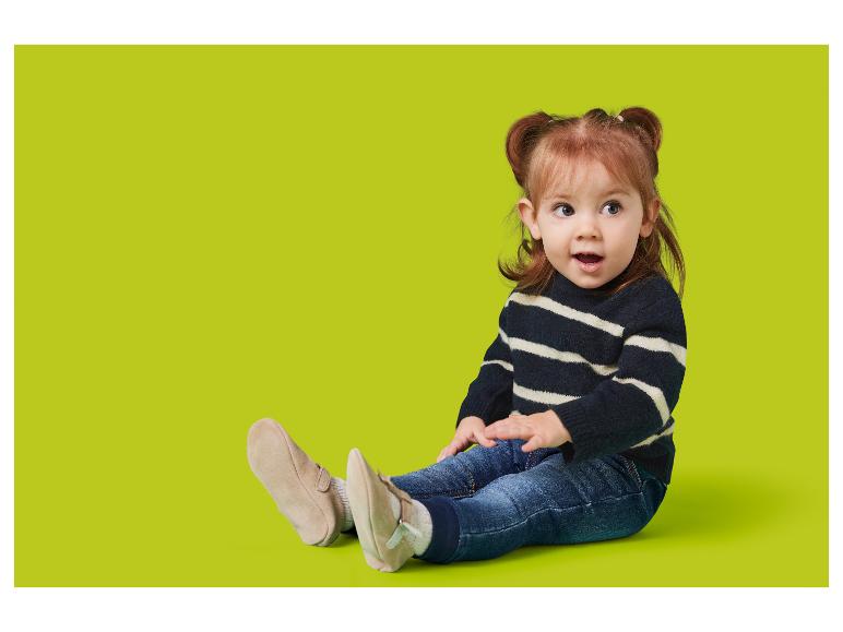 Un tout-petit en pull rayé et jean est assis sur un fond vert lime.