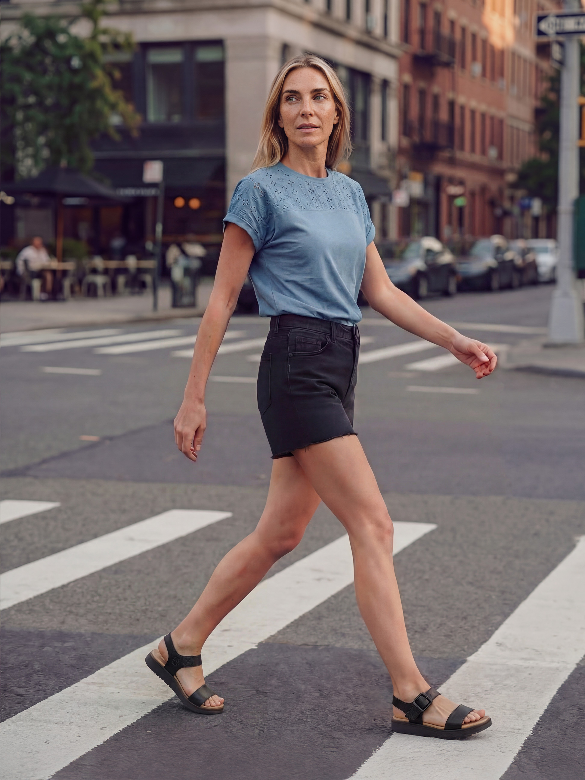 Femme en t-shirt bleu et short noir traversant la rue sur un passage piéton.
