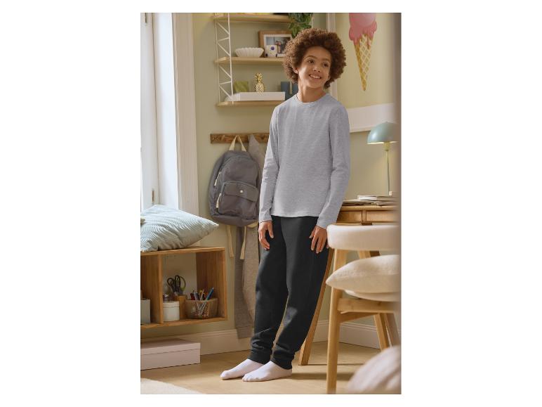 Jongen in grijs shirt met lange mouwen en zwarte joggingbroek in een kamer.