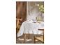 Wit tafelkleed met ruches op een tafel met servies en glazen, omringd door houten stoelen.