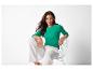 Femme en chemisier vert et pantalon blanc, assise sur une chaise blanche.