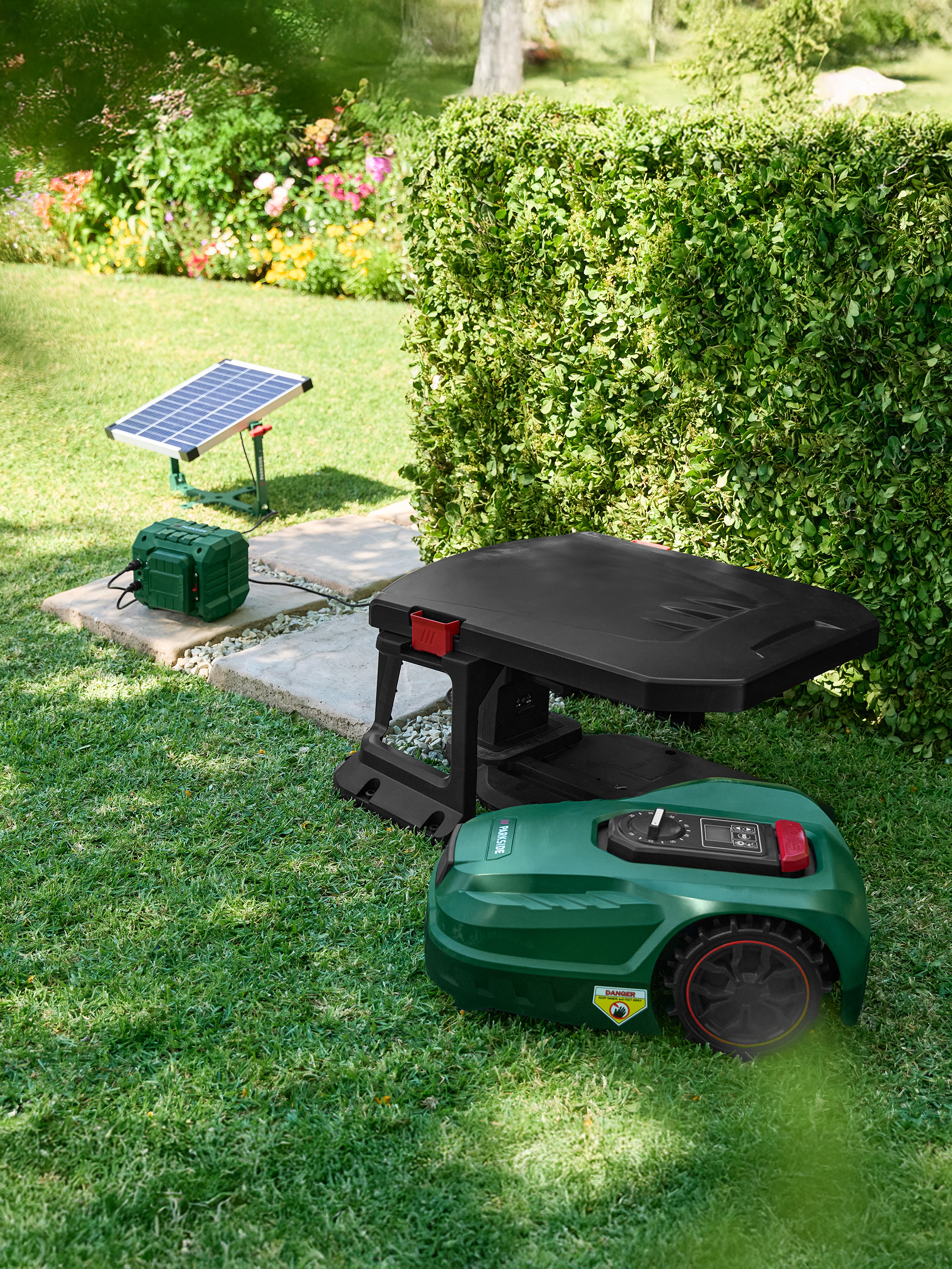 Tondeuse robot avec station de charge et panneau solaire dans un jardin.