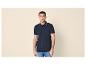 Man in marineblauw poloshirt met blauwe streepdetails en jeans.