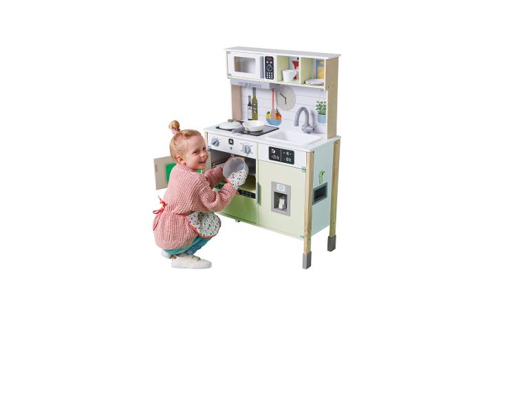 Lachend meisje in schort stopt een schaal in de oven van een houten speelkeuken.