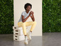 Une femme portant un t-shirt gris et un pantalon jaune est assise sur une caisse en bois et porte des bottes blanches.