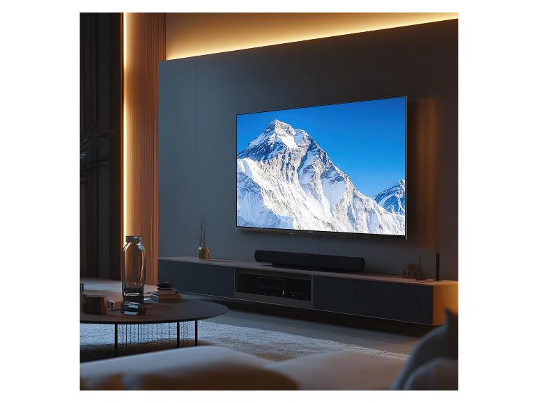 Woonkamer met een grote tv die een besneeuwd berglandschap toont en een soundbar.