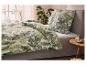 Bed met dekbedovertrek en kussen met tropisch bladpatroon, een plant en een bijzettafel.
