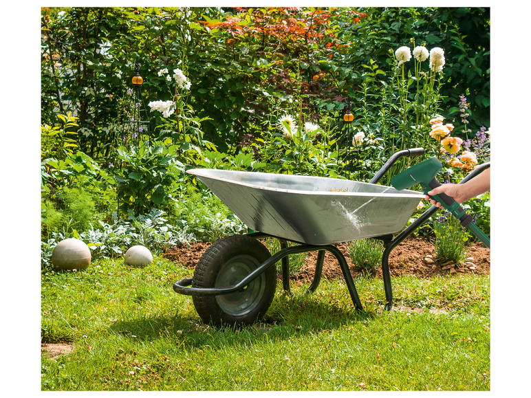 Een tuinslang met sproeikop wordt gebruikt om een ​​tuinwagen in een tuin te vullen.