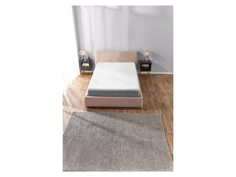 Un lit rose avec un matelas blanc et un tapis gris.