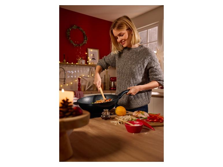 Lachende vrouw kookt roerbakgerecht in een wok, met verse ingrediënten op het aanrecht.