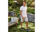 Man in een wit polo shirt en beige shorts in een tuin.