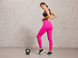 Een vrouw in roze leggings en zwarte sportschoenen met een kettlebell op de grond