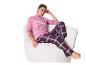 Vrouw in roze pyjama met print en geruite broek, zittend in een fauteuil.