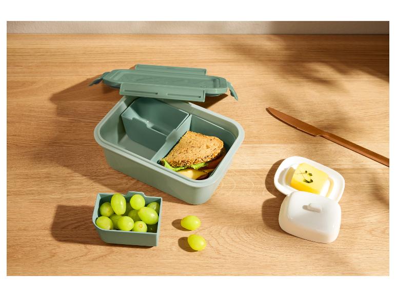 Boîte à lunch verte avec un sandwich et des raisins sur une table en bois.