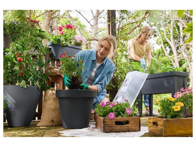Twee vrouwen planten bloemen en groenten in potten en verhoogde bedden in de tuin.