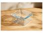 Trois récipients en verre carrés empilés avec un rebord bleu sur une table en bois.