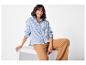 Femme en chemise rayée bleu et blanc et pantalon marron assise et souriante.