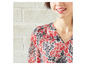 Een vrouw draagt een roze blouse met bloemenprint en een zilveren ketting.