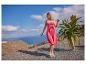 Femme en robe d'été rose et sandales, debout en extérieur au bord de la mer avec une plante d'aloès.
