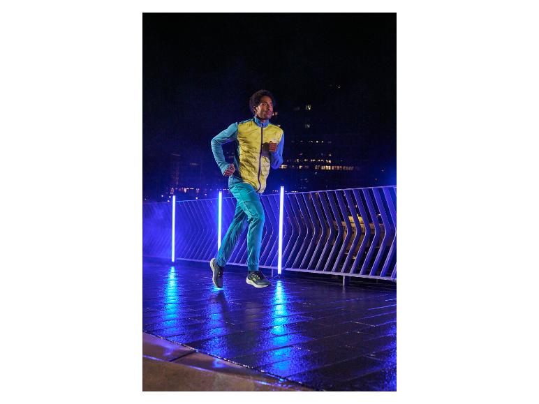 Un homme court en jogging bleu et veste jaune sur un balcon éclairé.