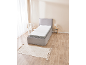 Grijs boxspringbed met wit matras in slaapkamer met houten vloer en beige vloerkleed.