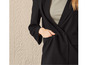 Een vrouw draagt een zwarte blazer met een beige top eronder.