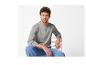 Homme aux cheveux bouclés portant un t-shirt gris à manches longues et un jean bleu, assis sur une chaise.