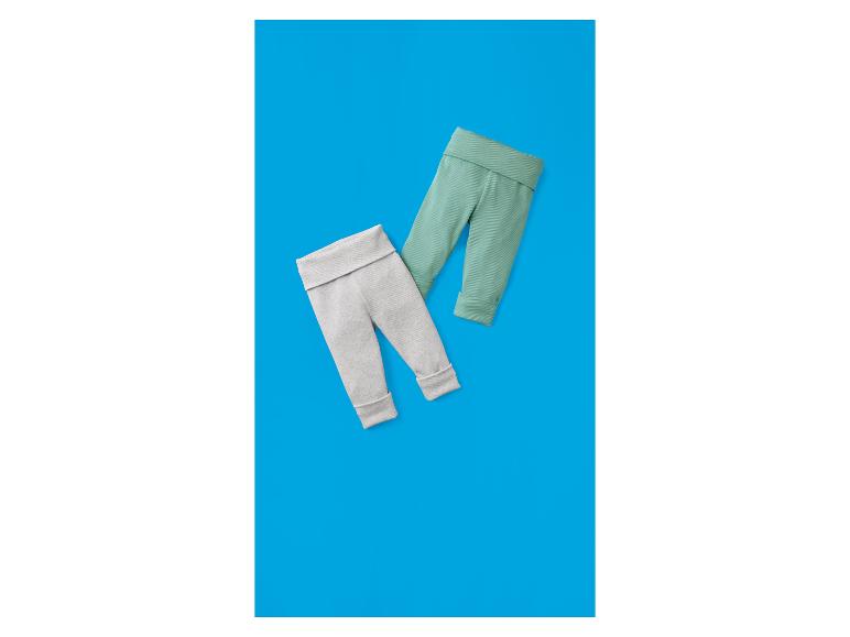 Twee paar baby leggings, één grijs en één mintgroen, op een blauwe achtergrond.