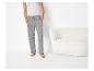 Man in grijze joggingbroek en wit hemd, staand naast een witte fauteuil.