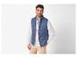 Lachende man in een blauw gewatteerd vest, wit overhemd en beige broek.